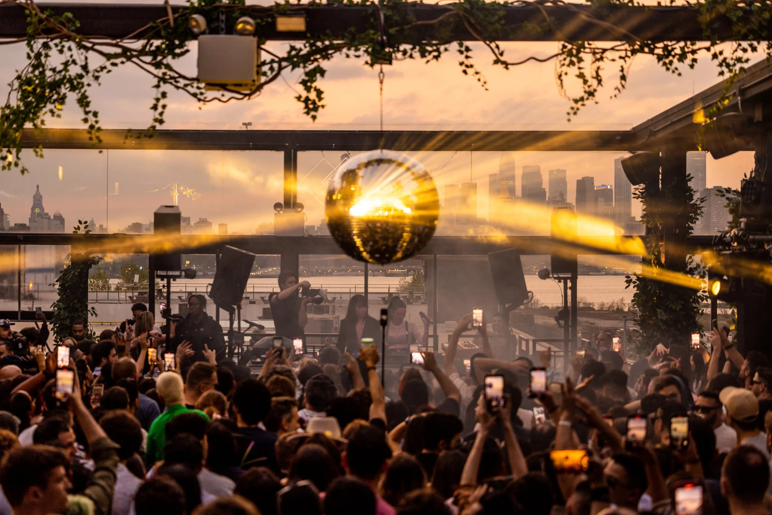 DJs and a packed crowd on the Superior Ingredients rooftop at sunset, with the Manhattan skyline behind them.
